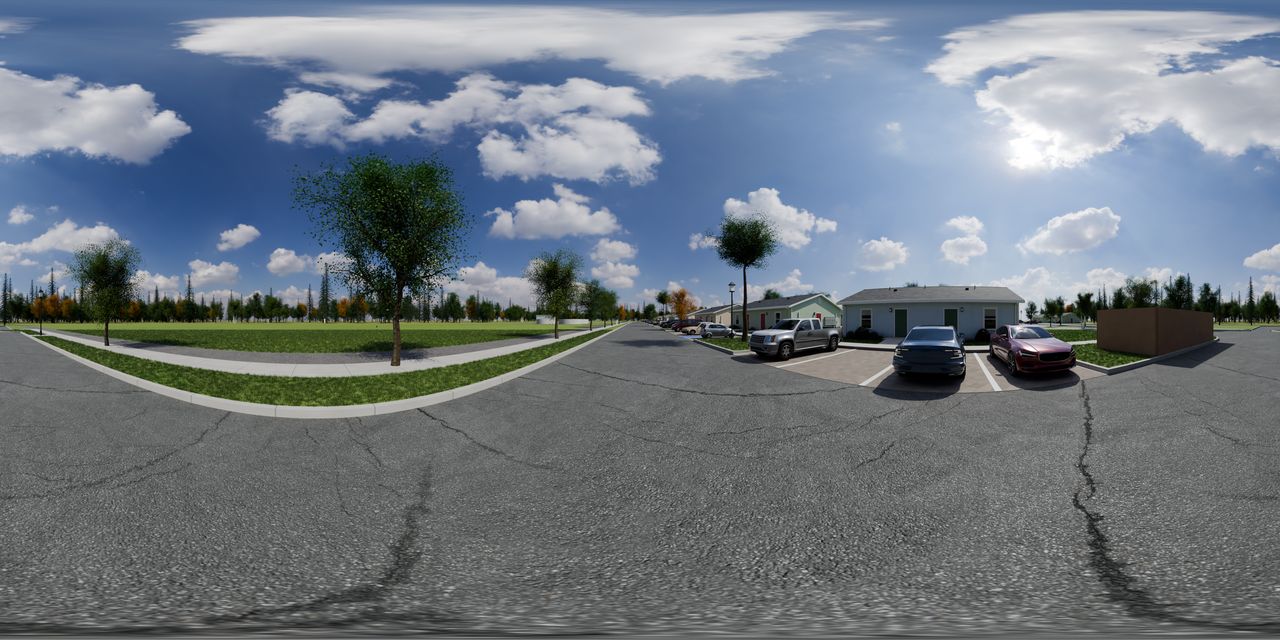 A paved lane with cars parked in front of one-story homes, a grass strip and trees on the far side, and an open field beyond.